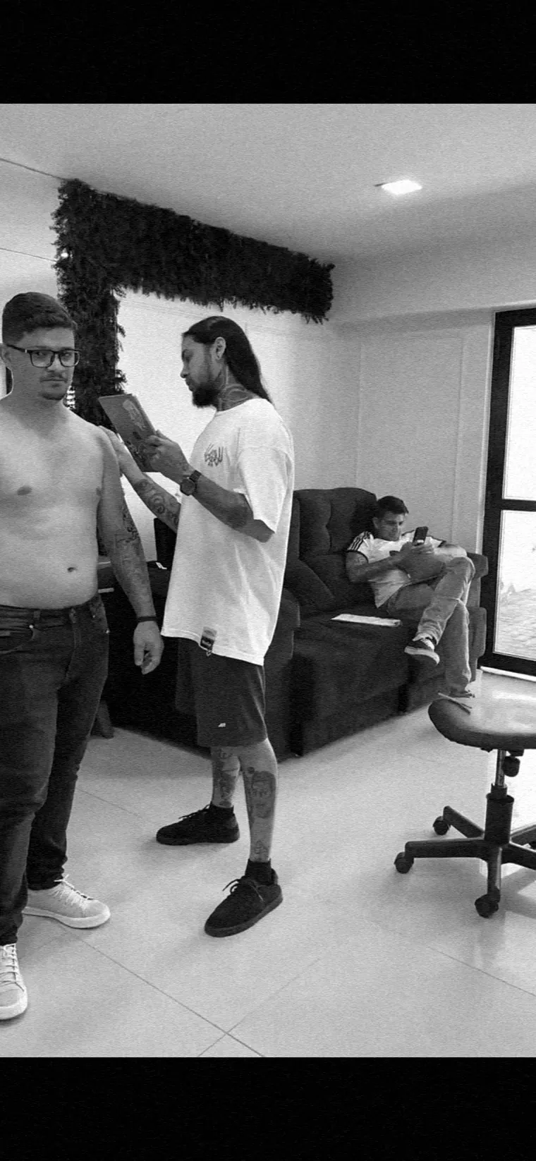Michael Douglas de pé no estúdio, segurando e medindo o braço do cliente antes do projeto